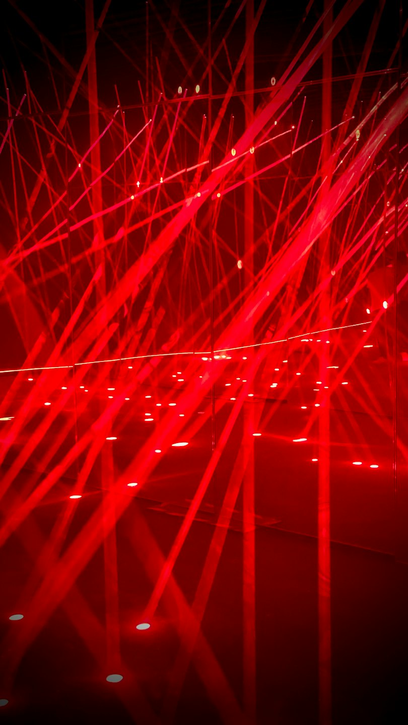 Rote Laserstrahlen kreuzen sich auf einem spiegelnden Hallenboden.