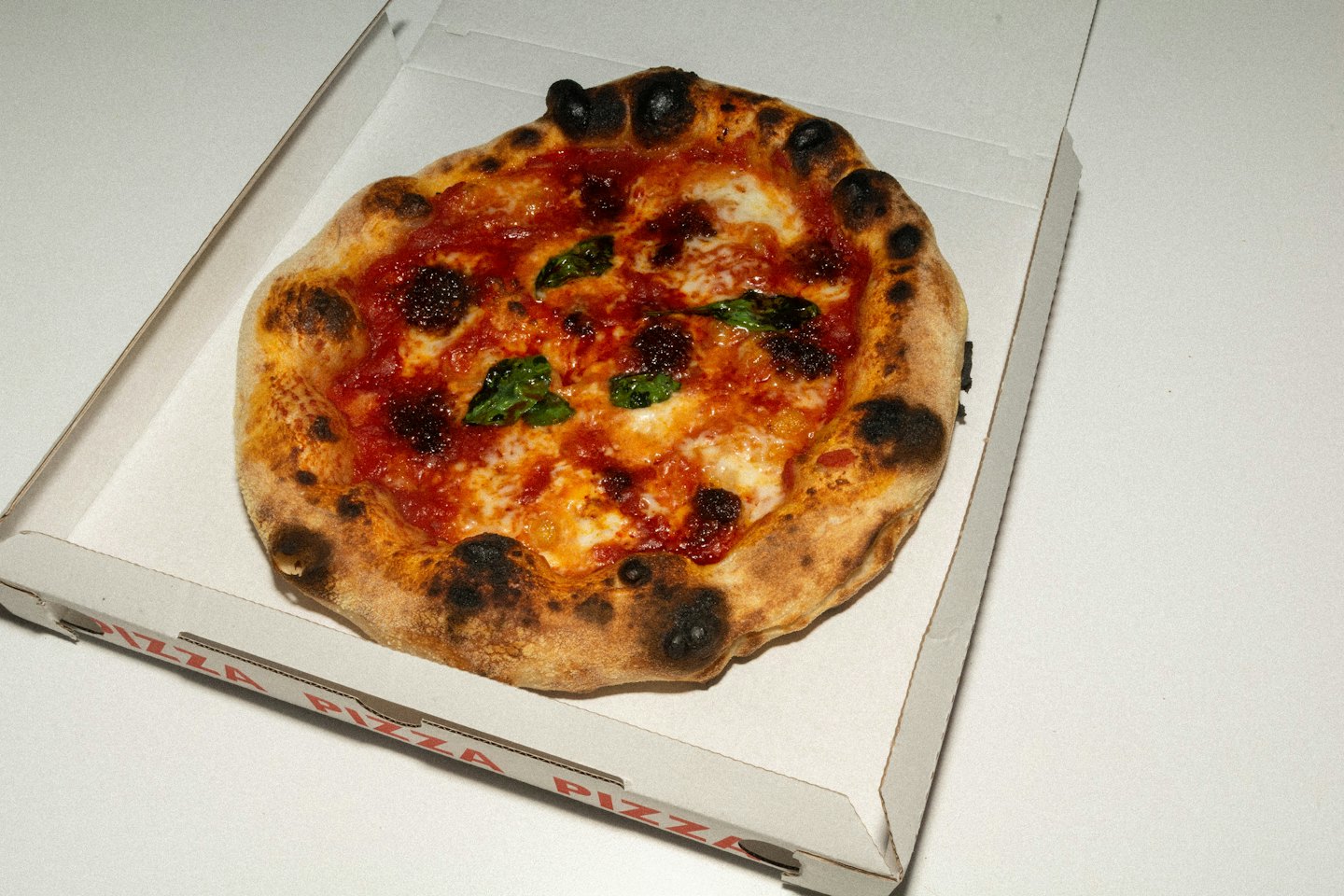 Frisch gebackene Pizza mit Basilikum in einer Lieferbox.