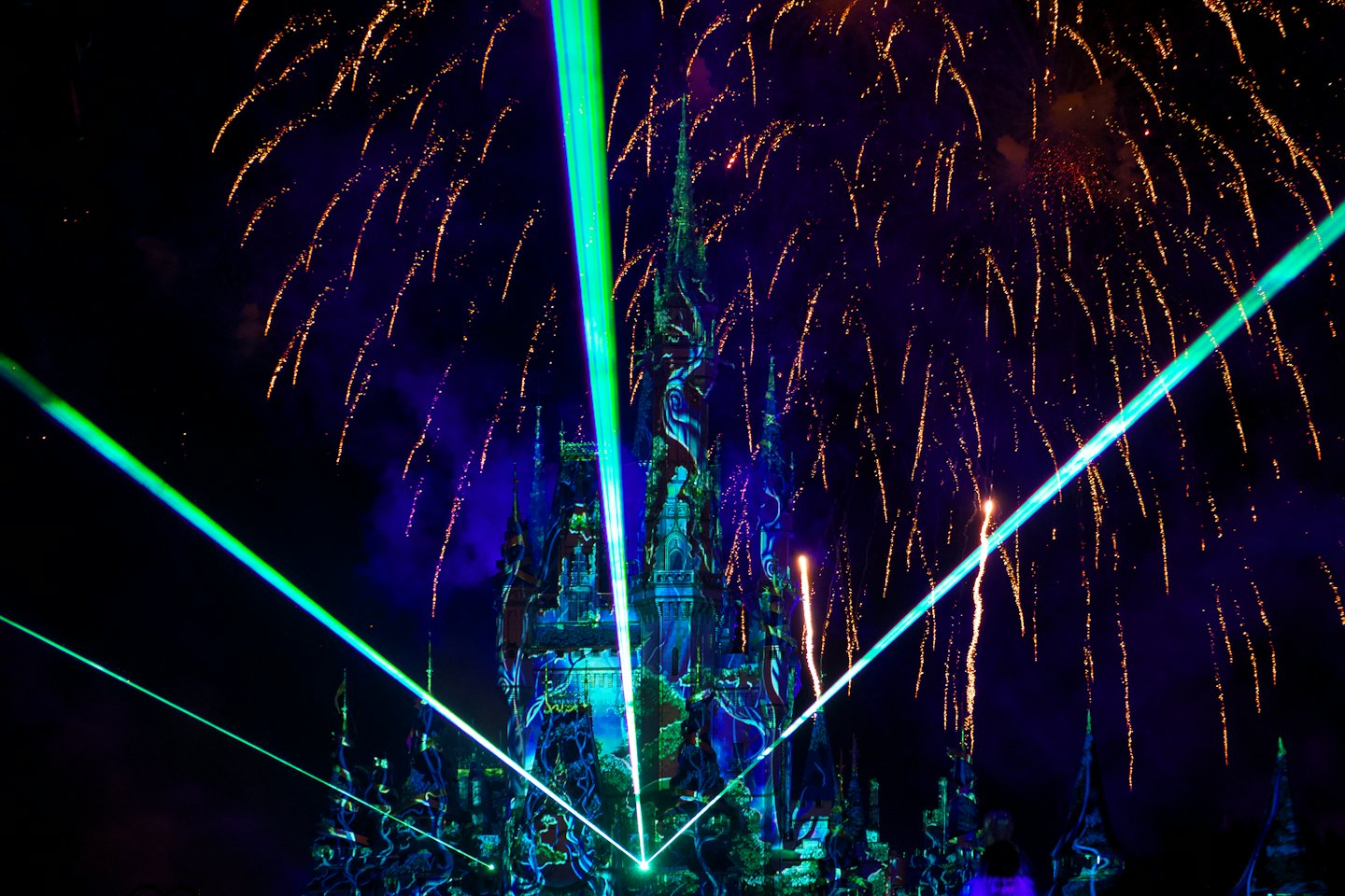 Bunte Feuerwerkskörper und Laserstrahlen beleuchten eine Fantasieburg bei Nacht.
