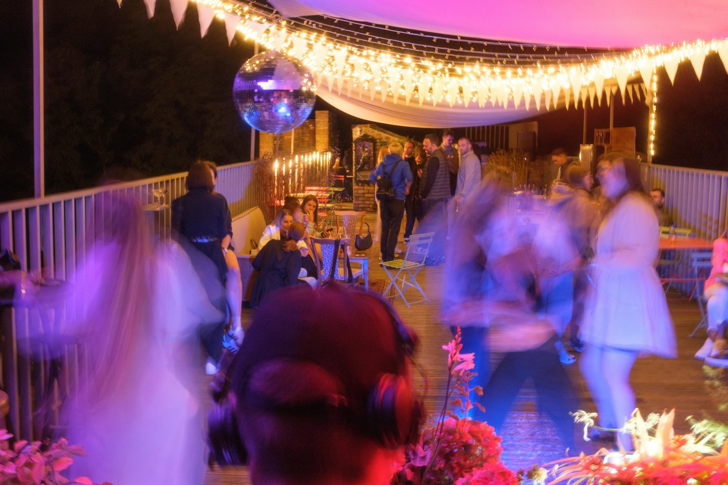 Discokugel und Lichterketten beleuchten eine lebhafte Gartenparty auf einer Terrasse.