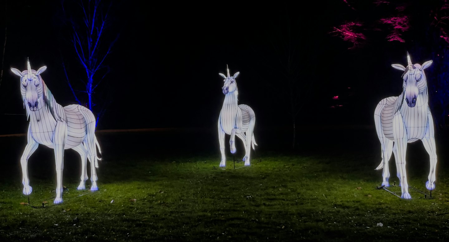 Drei leuchtende Einhorn-Skulpturen stehen nachts auf einer Rasenfläche.